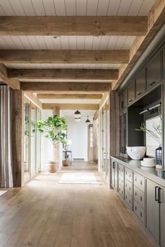 a long hallway with wooden floors and cabinets on both sides is lined with potted plants