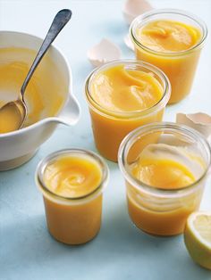 four jars filled with orange curd next to sliced lemons