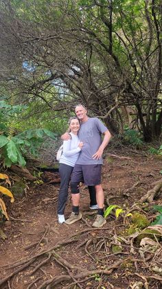 a man and woman standing in front of trees with their arms around each other on a dirt path