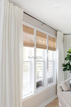 a living room with white drapes and curtains on the windowsills, in front of a large potted plant