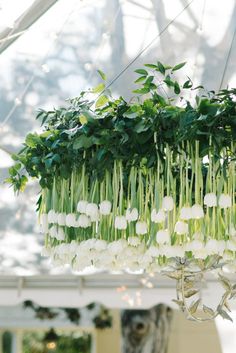 a chandelier with white flowers and greenery hanging from it's sides