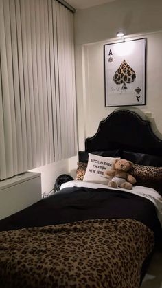 a teddy bear sitting on top of a bed next to a window with blind shades