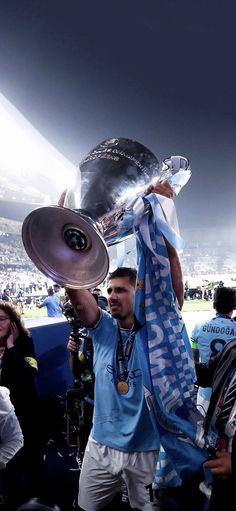 a man holding up a silver trophy in front of a crowd at a soccer game