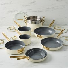 an assortment of white and grey dishes with gold handles on a marble countertop in the shape of a circle