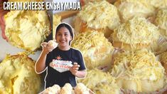 a woman holding up some food in front of a bunch of muffins with cheese on them