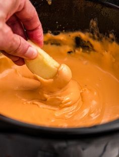 a person dipping an apple into sauce in a black bowl with a wooden spatula