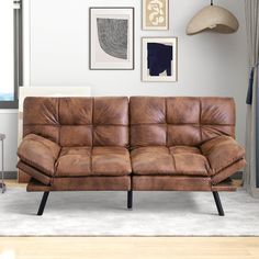 a brown leather couch sitting on top of a hard wood floor next to a window