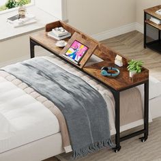 a bed with a laptop on top of it next to a table that has an ipad