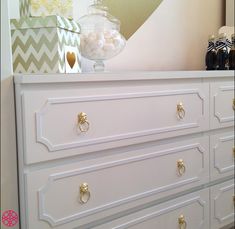 a white dresser with gold handles and knobs next to a vase filled with candy