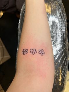 a woman's arm with four small flowers tattooed on the left side of her arm