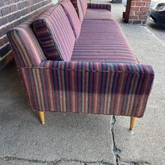 a striped couch sitting on top of a sidewalk next to a brick wall and door