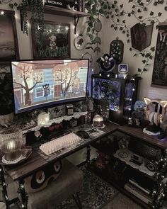 a computer desk topped with a monitor next to a wall covered in pictures and plants