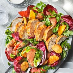 a white plate topped with salad and meat on top of a table next to silverware