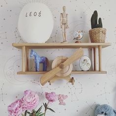 two wooden shelves with toys on top of them next to pink flowers and succulents