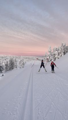 two cross country skiers going down a snow covered trail in the woods at sunset