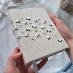 a person holding a small book covered in tiny white sheep on top of a table