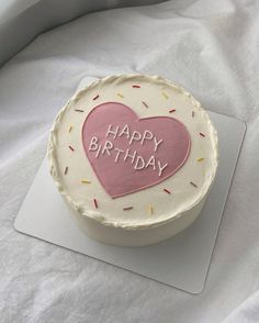 a birthday cake that is on top of a white table cloth with pink frosting and sprinkles