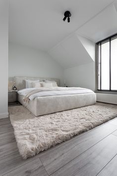 a large white bed sitting in the middle of a bedroom next to a tall window