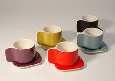 four different colored cups and saucers sitting next to each other on a white surface