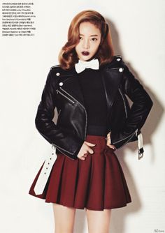 a woman in a red skirt and black jacket with a bow tie standing next to a white wall