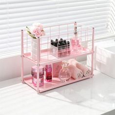 a pink shelf with bottles, soaps and other items on it in front of a window