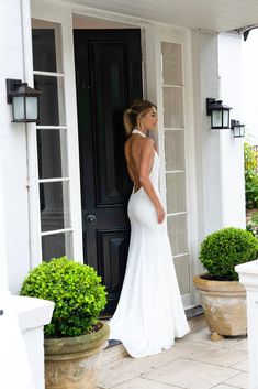 a woman standing in front of a black door wearing a white wedding dress with open back