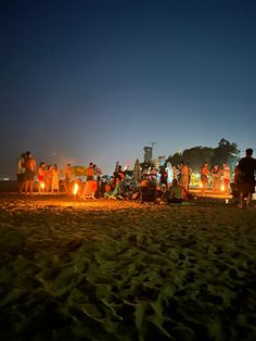 a group of people standing on top of a sandy beach next to the ocean at night