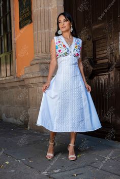 a woman standing in front of a building wearing a white dress with flowers on it