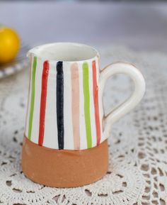 a striped mug sitting on top of a doily next to a plate with lemons