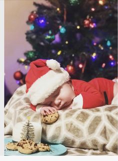 a baby wearing a santa hat laying on top of a bed next to a christmas tree