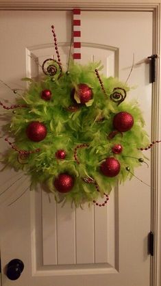 a green wreath with red ornaments hanging on the front door