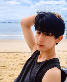 a young man sitting on top of a beach next to the ocean with his hair blowing in the wind