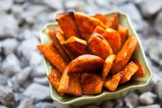 a green bowl filled with sweet potato wedges sitting on top of a pile of rocks