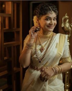 a woman in a white sari talking on a cell phone while wearing gold jewelry