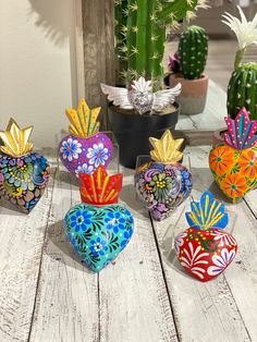 colorful heart shaped vases sitting on top of a wooden table next to cacti