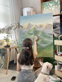 a woman is painting on an easel with a dog sitting in front of her