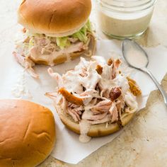 two pulled pork sandwiches with coleslaw and mayonnaise next to a glass of milk