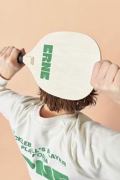 a man holding a paddle over his head while wearing a white shirt with green print on it