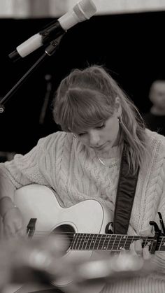 a young woman playing an acoustic guitar in front of a microphone with her eyes closed