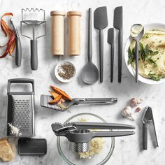 various kitchen utensils are arranged on a marble counter top with garlic, carrots and other ingredients