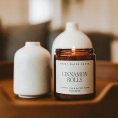 a candle sitting on top of a wooden table next to a white bottle filled with cinnamon rolls