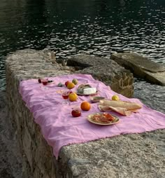 a table with food on it sitting next to the water in front of some rocks