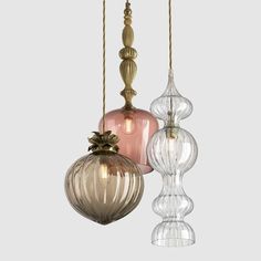 three glass pendant lights hanging from the ceiling in different shades of pink, gold and clear