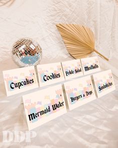 place cards for cupcakes, cookies and other treats on a bed with a fan