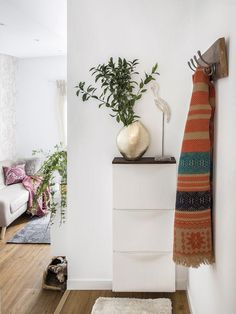 a living room with white walls and wooden flooring, a plant on top of a dresser