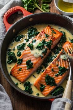 two salmon fillets with cream sauce and spinach in a skillet on a wooden table