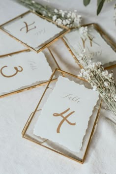 wedding table numbers displayed in gold frames with flowers and greenery on white linens