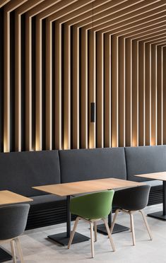 an empty restaurant with wooden walls and black benches, green chairs, and gray couches