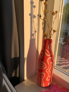 a red vase with flowers in it sitting on a window sill next to a pink rug