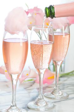 two champagne flutes filled with pink liquid being poured into wine glasses on a marble table